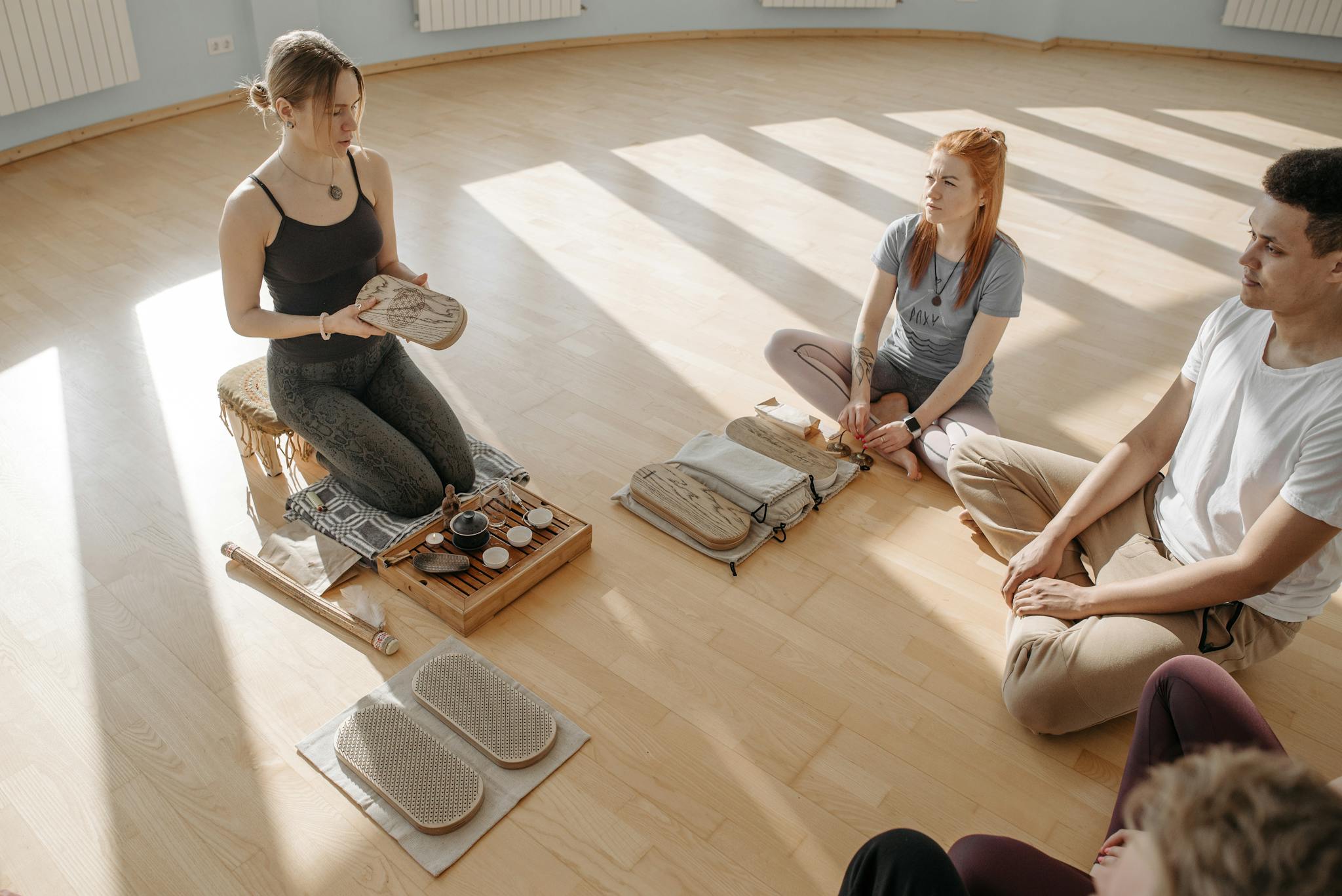 A diverse group participates in a tea ceremony and meditative session indoors on wooden flooring.