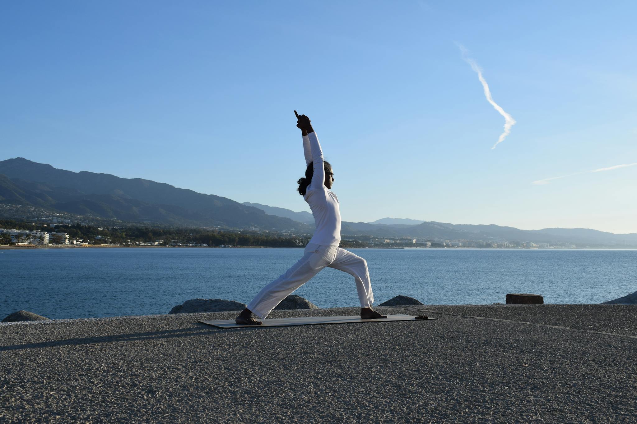 About A man doing yoga on a mat by the ocean under a clear blue sky.