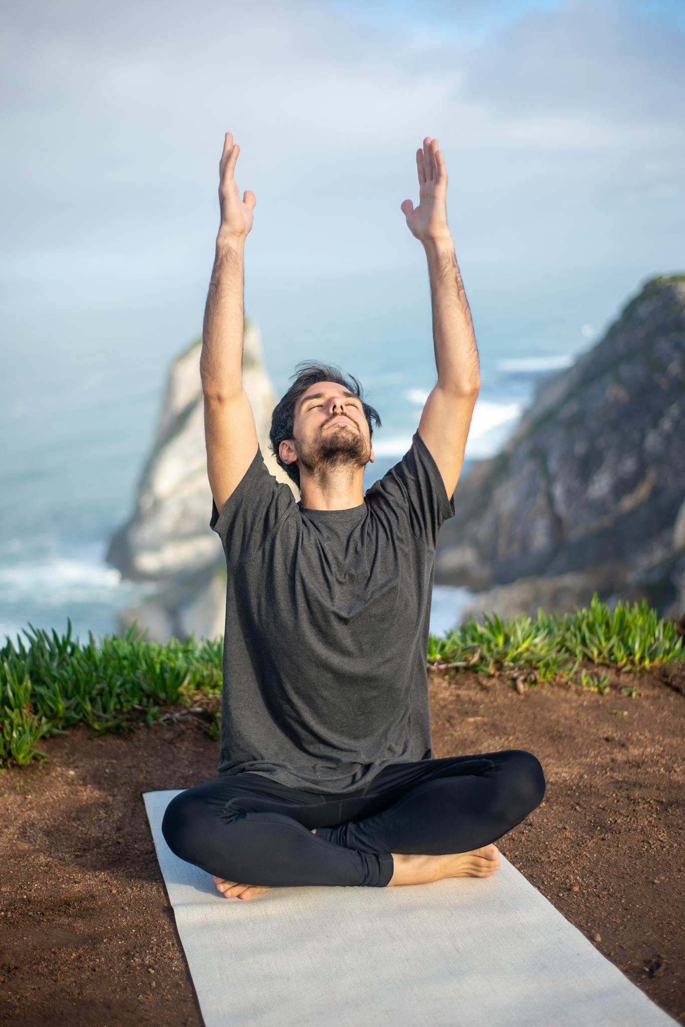 Man practicing yoga near the ocean, reaching upwards in a serene outdoor setting.