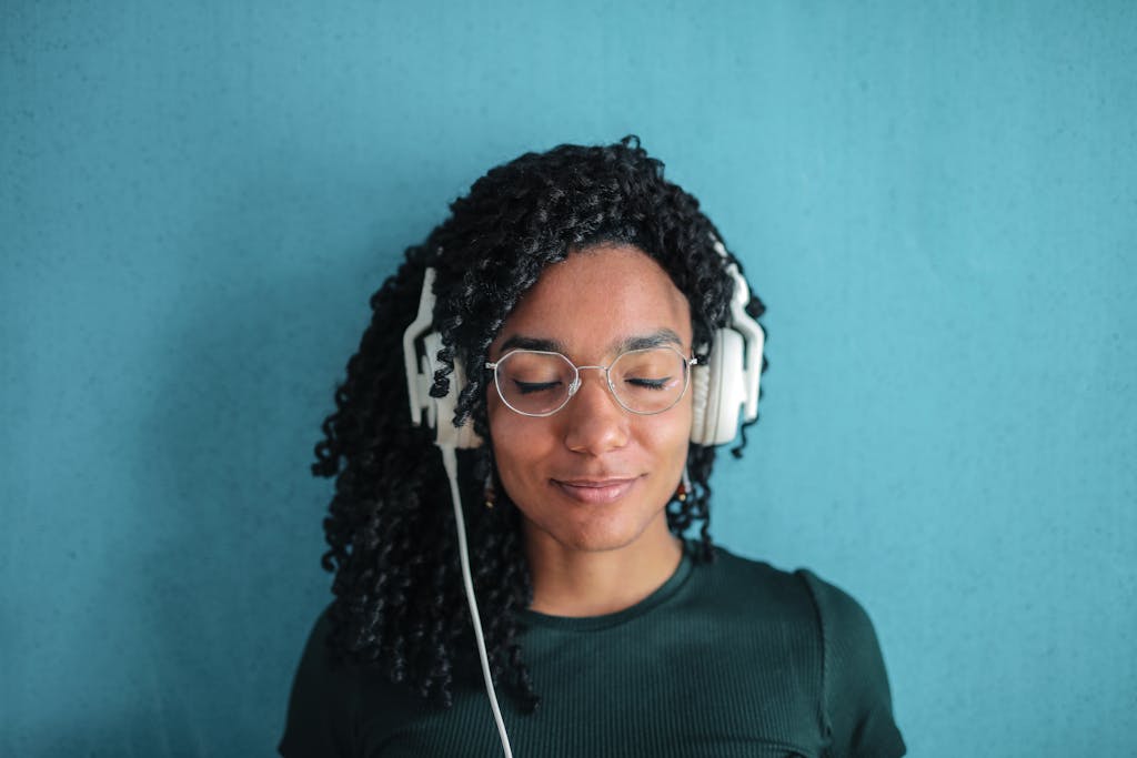 Portrait of a woman with headphones and glasses enjoying music against a blue background.