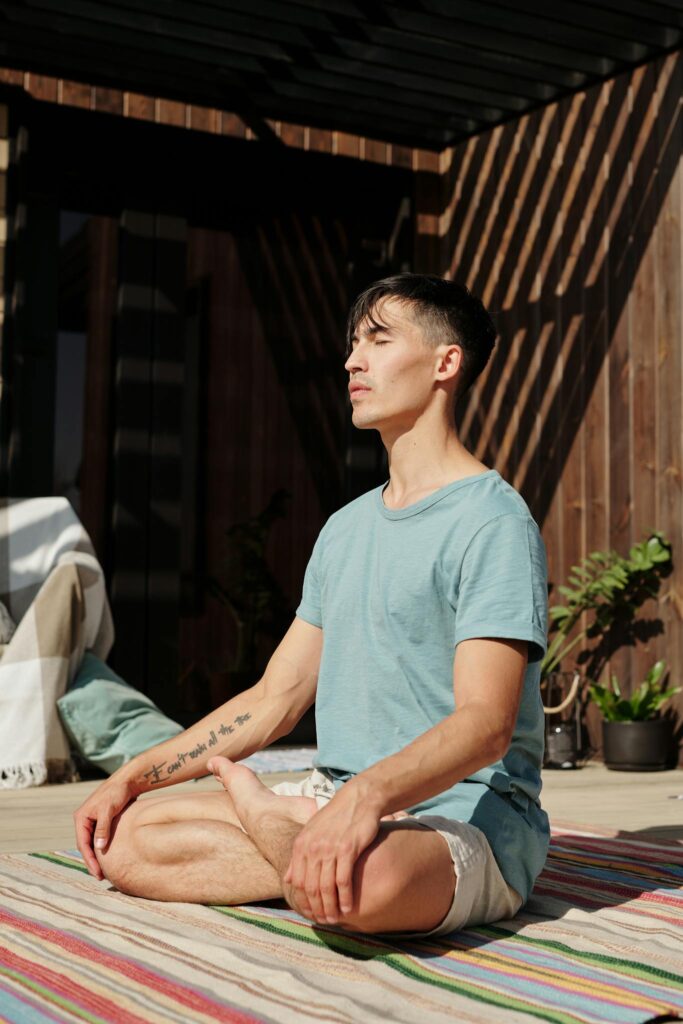 Young man practicing yoga outdoors, sitting cross-legged with eyes closed, embracing tranquility.