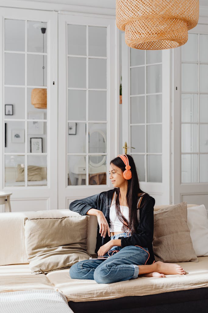 Young woman enjoying music with headphones on a cozy sofa in a bright, modern living room.